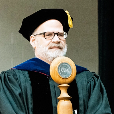 A photo of Dr. Richard Bilsker, holding the CSM College Mace at the 2024 Spring Commencement