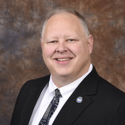 Professional headshot of CSM adjunct math and engineering professor Dr. William Bassett. He is smiling at the camera and wearing a dark colored suit and tie. 