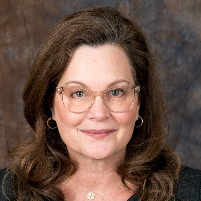 A professional headshot of a smiling woman with long black hair, wearing a dark outfit.